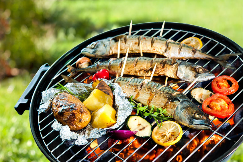 grilled mackerel fish with baked potatoes over the coals on a barbecue