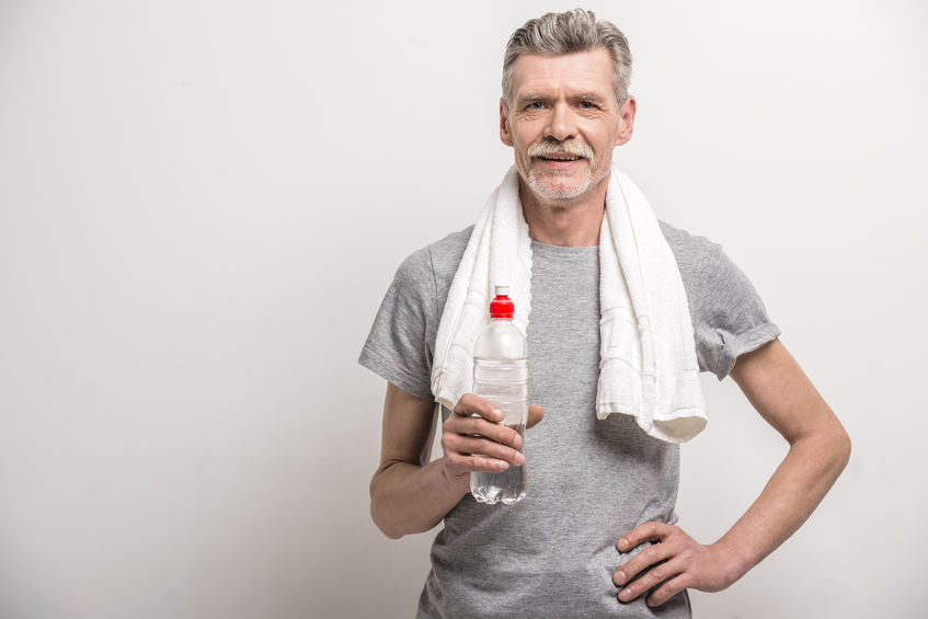 smiling senior man in t-shirt on neck towel with bottle water on grey background.