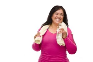 middle aged hispanic woman in workout clothes with water bottle and towel against a white background.
