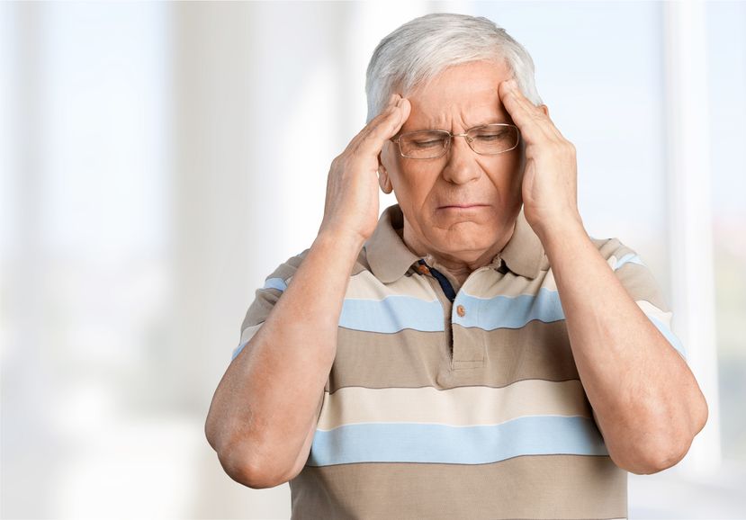 an elderly man rubbing his temples because he's having a stroke