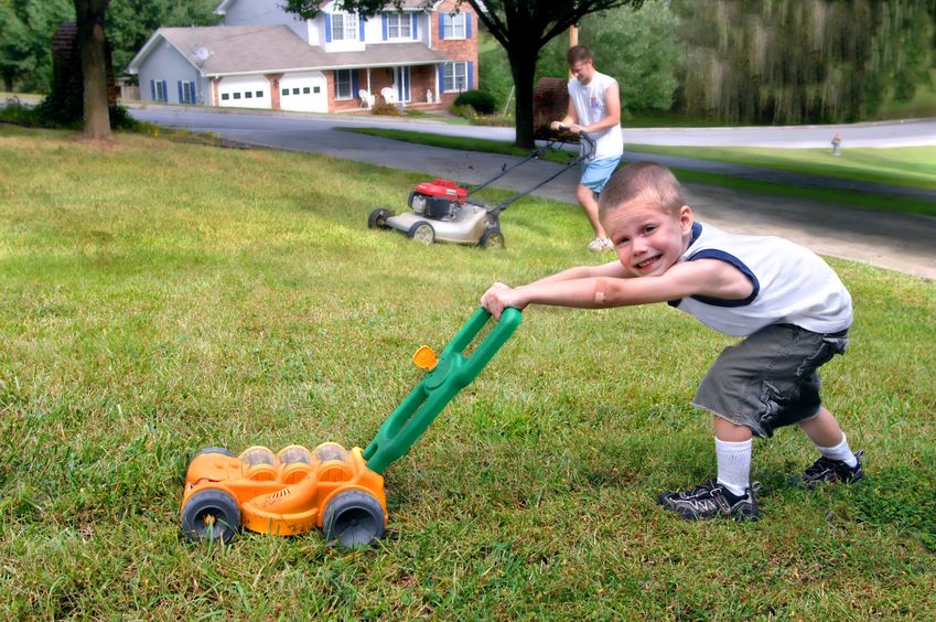15024786 - small boy mows grass just like his dad. he is grinning and pushing a toy lawn mower while dad mows with his.