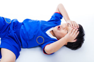 42044674 - sports injury. youth asian (thai) soccer player in blue uniform painful. child closed eyes and touching his forehead. on white background. studio shot. boy lie down. top view