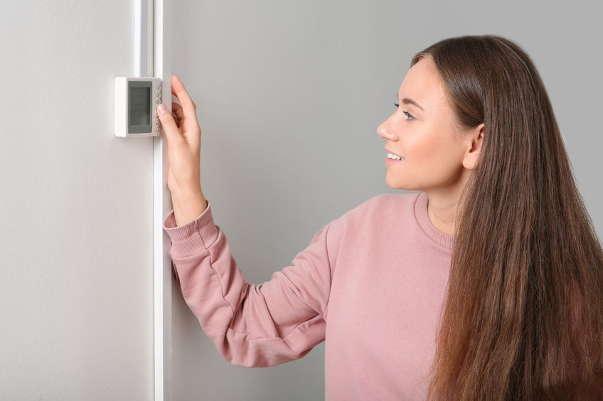 Woman adjusting thermostat on white wall. Heating system