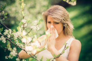Woman with pollen allergy in springtime near tree in bloom.
