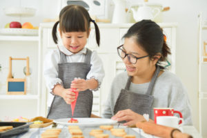 Asian child and young mother decorating cookies.