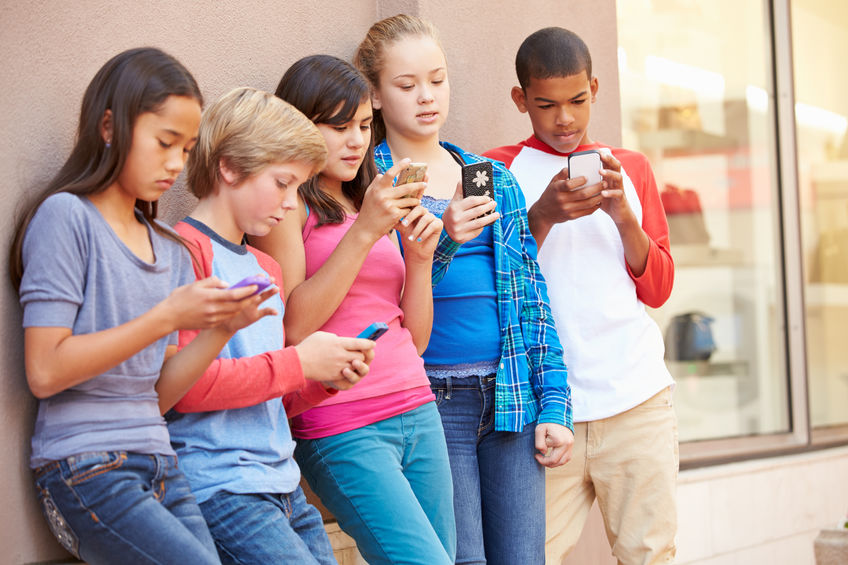 Group Of Children Sitting In Mall Using Mobile Phones