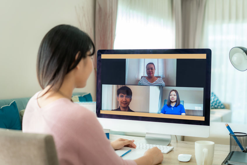 Back view of Asian business woman talking to her colleagues about plan in video conference. Multiethnic business team using computer for a online meeting in video call. Group of people smart working from home.