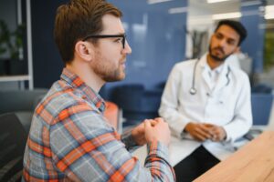 medicine, healthcare and people concept - indian doctor giving prescription to male patient at clinic.