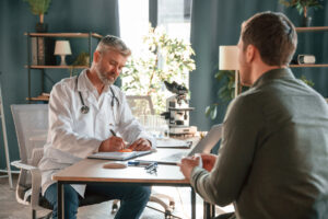 Senior doctor that is in coat is consulting a patient in the clinic.