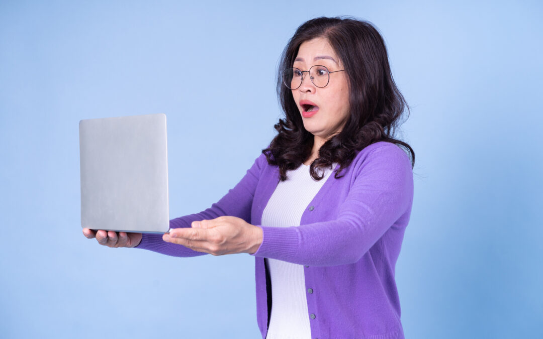 Middle aged Asian woman using laptop on blue background getting incorrect healthcare information from social media influencers who are sharing incorrect information