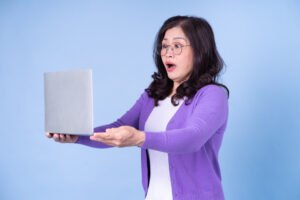 Middle aged Asian woman using laptop on blue background getting incorrect healthcare information from social media influencers who are sharing incorrect information