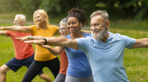 Group of diverse seniors led by young instructor practicing warrior yoga pose outdoors, happy elderly people promoting inclusivity and wellness, exercising in lush park setting, closeup shot