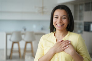 A grateful woman smiling and holding her hands over her heart in a gesture of gratitude.